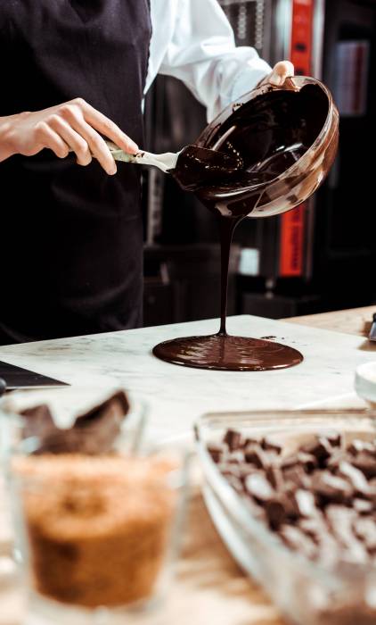 selective focus of chocolatier pouring melted chocolate on marble surface